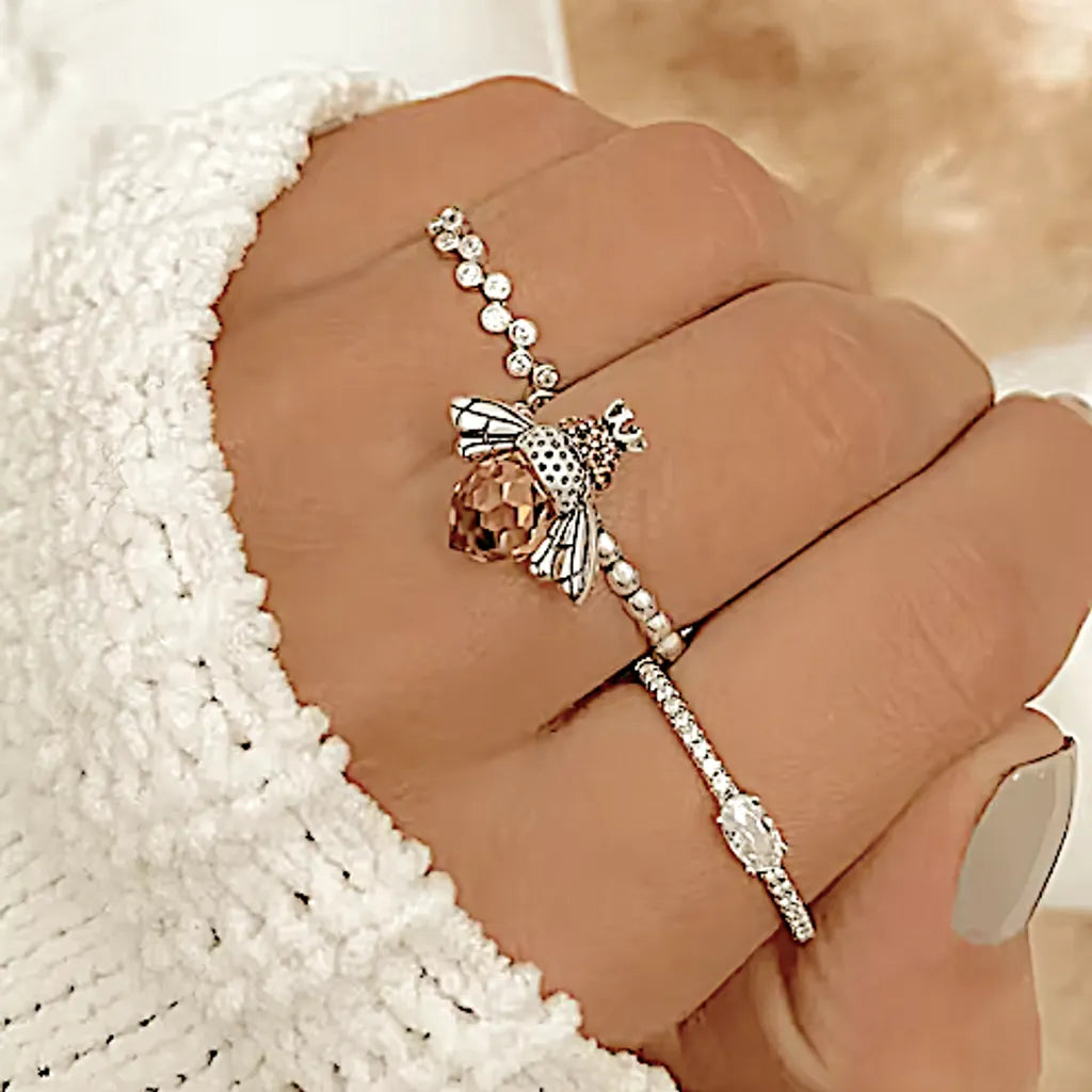 Vue rapprochée sur une main féminine ornée de la bague abeille en argent 925, associée à deux bagues avec pierres scintillantes, révélant le contraste délicat des textures et des reflets.