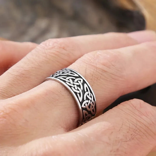 Bague Celte Tyr portée à la main gauche, en pleine lumière naturelle, soulignant les nœuds triquetra gravés sur un acier inoxydable à contraste élevé.