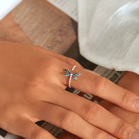 Bague libellule en argent 925 avec zircone blanche, portée sur une main féminine posée sur une table, mettant en valeur l'éclat du bijou.