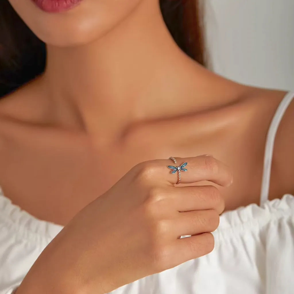 Bague libellule en argent 925 avec zircone blanche, portée à la main d'une femme à hauteur de sa poitrine, pour une mise en scène élégante.