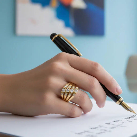 Gros plan de profil sur la bague Lyra en plaqué or 14K portée à la main. Le zoom révèle les quatre rangs évasés et leurs douze zircones entre l'éclat du stylo et un mur bleu ciel.