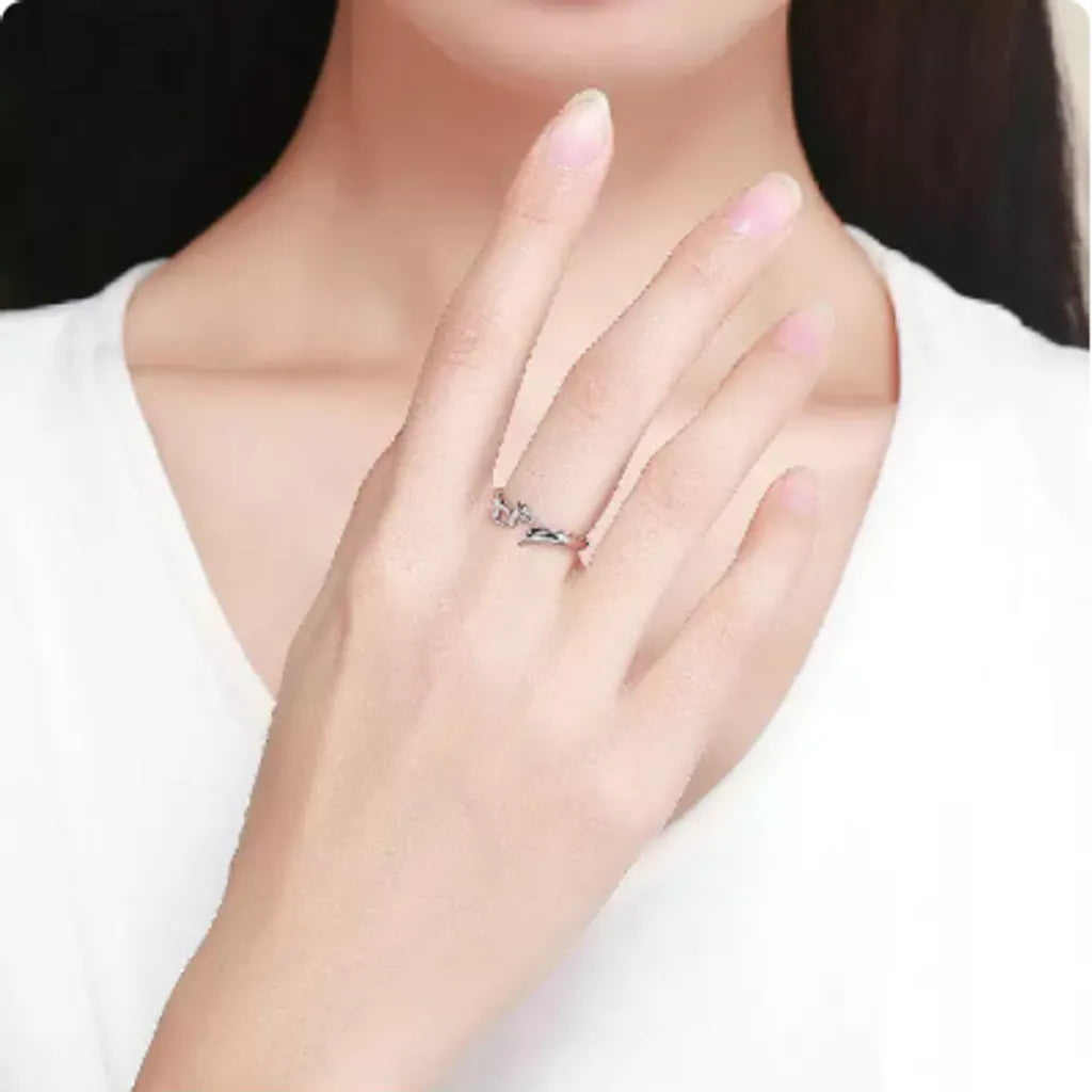 Main d'une femme portant une bague renard blanc en argent 925. La main est délicatement posée avec les doigts légèrement pliés, mettant en avant le design ouvert et subtil de la bague. La femme, habillée d'un haut blanc à col rond, offre un contraste élégant avec le bijou. Le fond clair accentue la pureté et le raffinement de la scène.