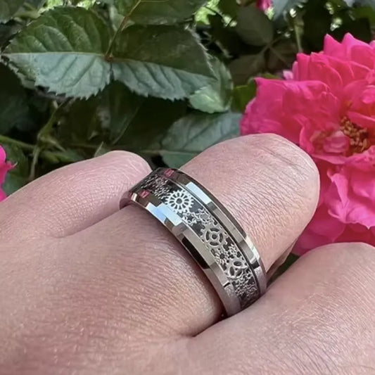 Bague roue dentée portée à l'annulaire, mise en scène florale avec roses pour souligner le contraste entre nature et design mécanique.