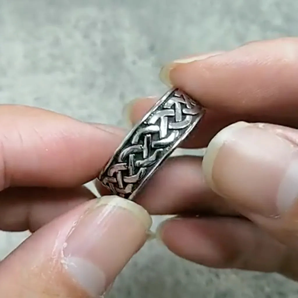 Bague Skeld portée entre les doigts, motif celte tressé en relief sur fond vieilli, design inspiré des symboles vikings.