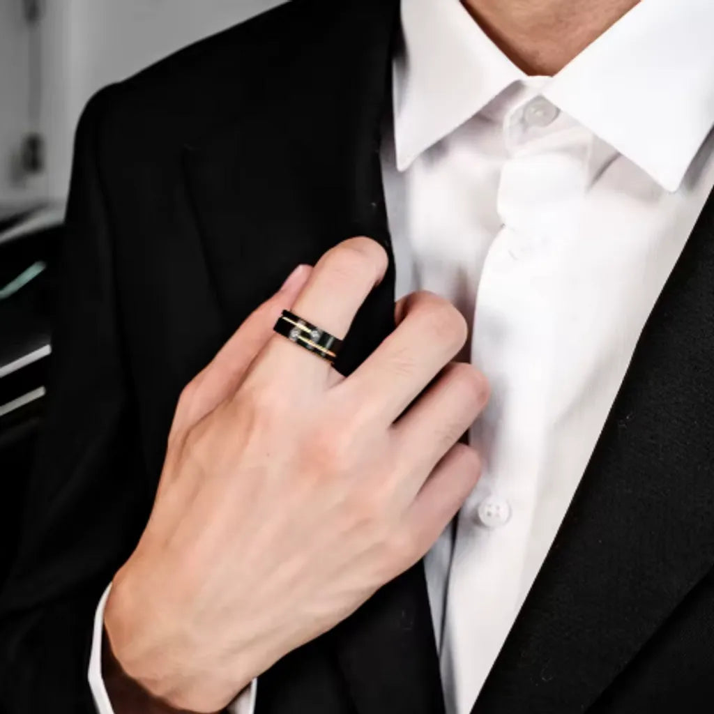Geste raffiné d’un homme en chemise blanche mettant en avant une bague Stella noire et dorée en acier inoxydable avec zircones brillantes.