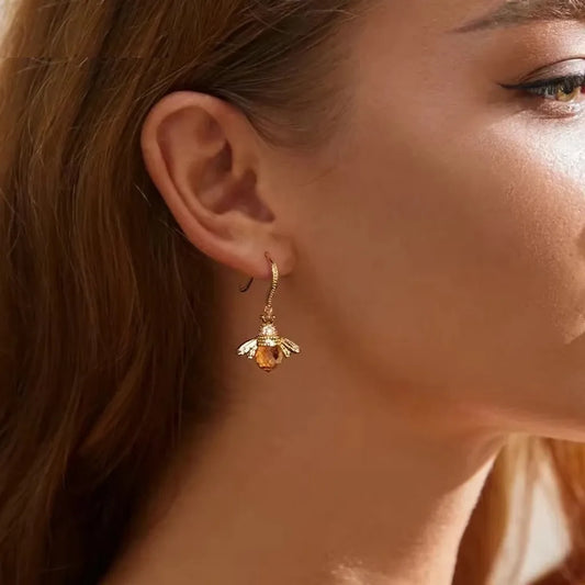 Boucles d’Oreilles Abeille Reine en argent 925 plaqué or, portées à l’oreille d’une femme en lumière dorée, éclat naturel du cristal facetté sur peau lumineuse.