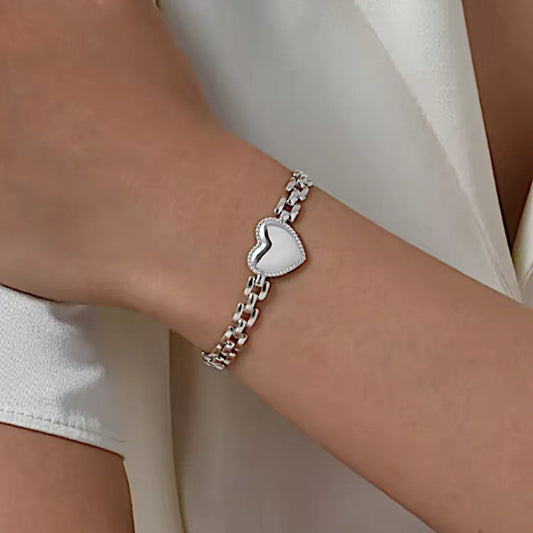 Bracelet Alma en acier argenté porté au poignet d'une femme élégante ; maillons graphiques et cœur central capturent la lumière pour un effet raffiné.