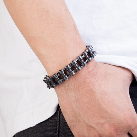 Bracelet biker chaîne de moto et fermoir en acier inoxydable présenté autour d'un poignet d'un homme le pouce dans la poche de son jean - coloris argent vieilli