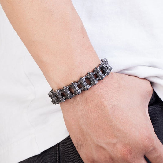 Bracelet biker chaîne de moto avec maillons de forme écrou hexagonal en acier inoxydable présenté autour d'un poignet d'un homme le pouce dans la poche de son jean - coloris argent vieilli