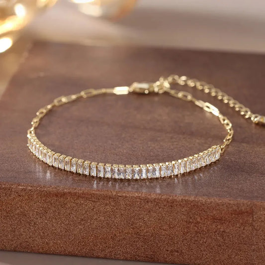 Gros plan du bracelet Clara doré en argent 925 sur bois, capturant les reflets doux des zircones sous lumière tamisée.