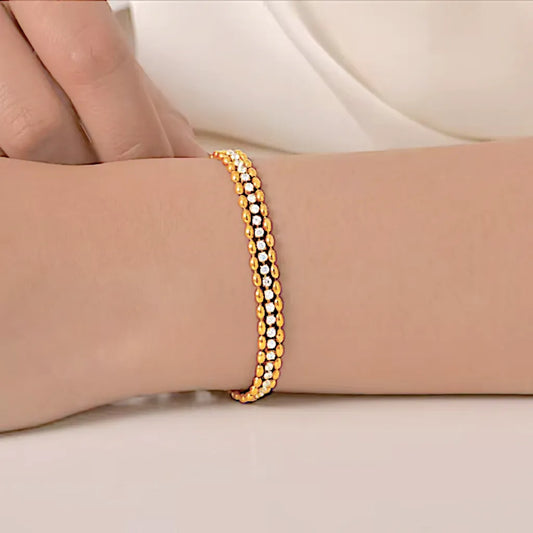 Le bracelet Elara doré porté au poignet, contraste chic sur peau nue, double chaîne perlée et éclat cristallin bien visibles.