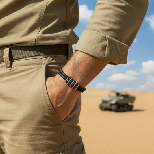 Très gros plan. Le bracelet Link cuir tressé noir et ses segments modulaires en acier, portés sur une tenue de trek kaki. Le design de l'assemblage s'accorde à l'équipement d'exploration.
