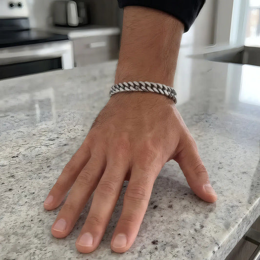 Bracelet maille cubaine 15 mm porté au poignet masculin sur un plan de travail en granit