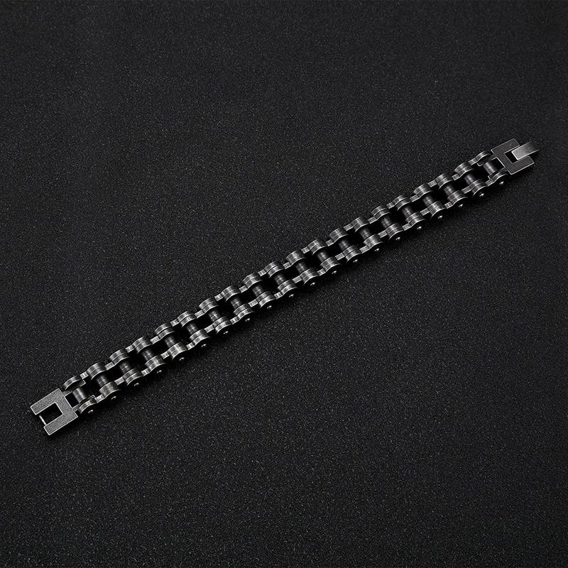 Vue de haut de toute l'étendu du bracelet ouvert biker à chaîne de moto et fermoir crochet à clip ouvert en acier inoxydable posé sur un plan de travail noir - coloris vintage de l'acier argent vieilli