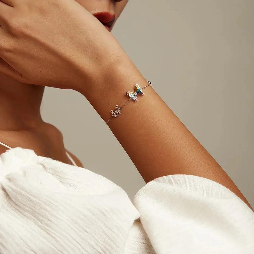 Bracelet Papilla en argent 925 porté sur poignet nu, avec détail visible des deux papillons, l’un coloré en émail, l’autre argenté.