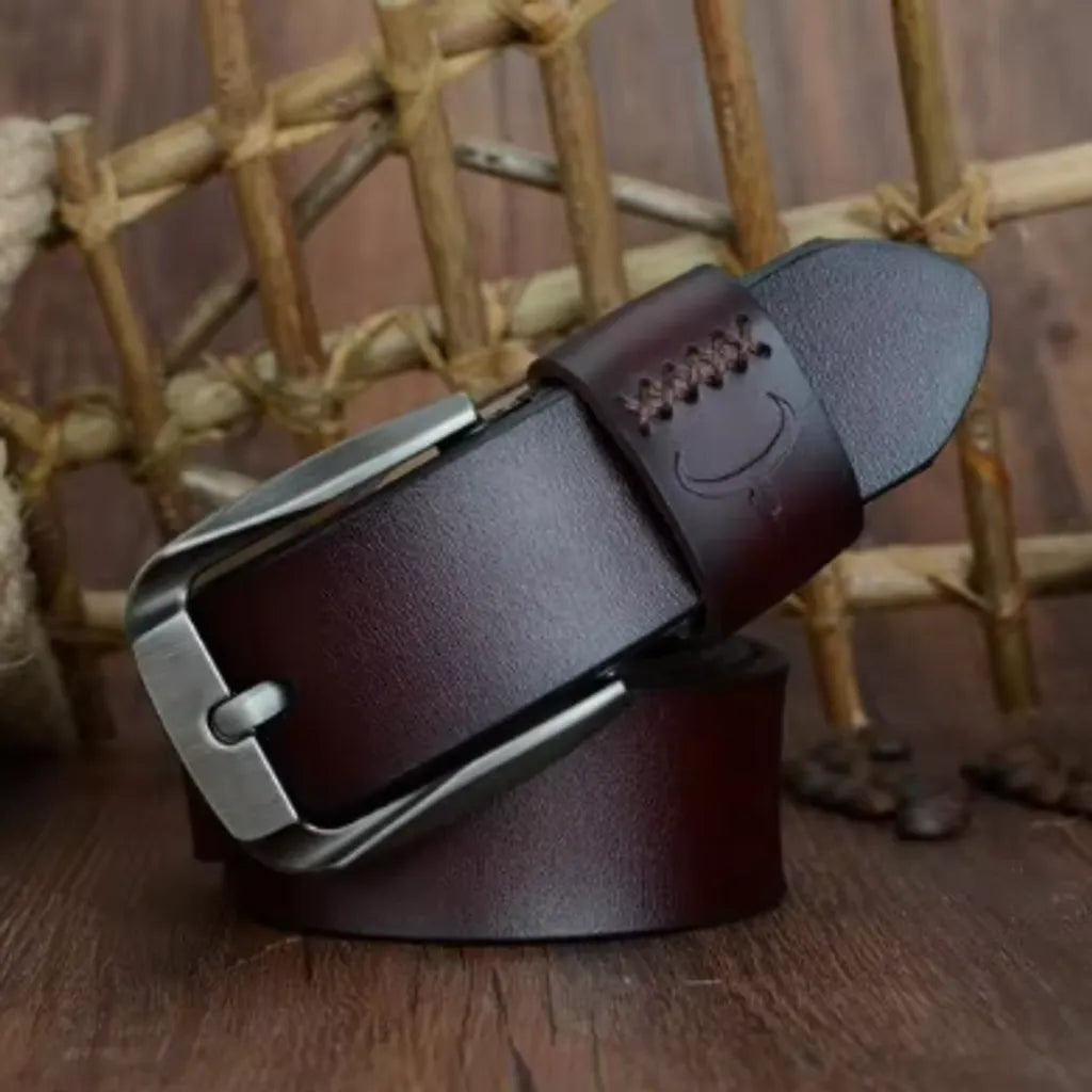 Ceinture vintage pour homme en cuir véritable lisse, bande de cuir de vache avec revêtement de protection. Sa boucle ardillon en métal est argentée et rectangulaire. Passant large cousu avec marquage corne de bovin - COWATHER. Présentation enroulée sur les lames d'un parquet en bois. Coloris lanière café.