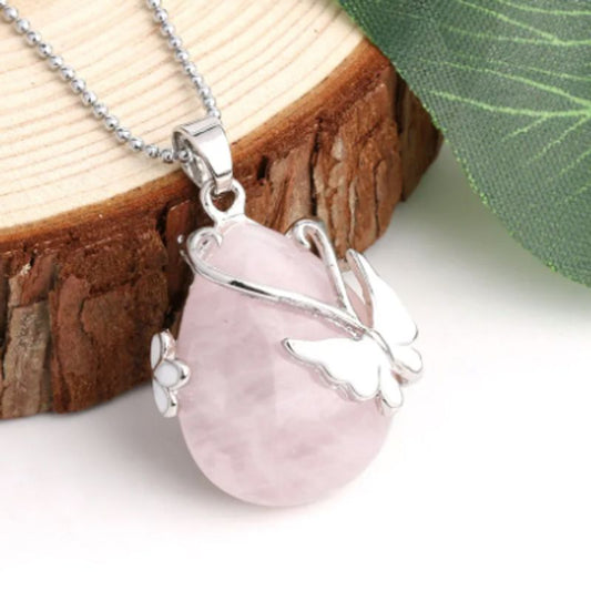 Collier chaine à bille avec pendentif goutte d'eau en pierre naturelle posé sur un rondin de bois - orné d'un papillon et d'une fleur en métal plaqué platine - pierre semi-précieuse quartz rose