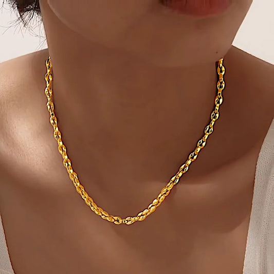 Collier doré porté de profil sur peau nue, reflets chauds captant la lumière douce.