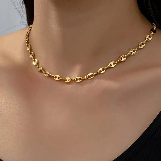 Le collier Nysa doré épouse délicatement la base du cou. Sa brillance contraste avec le décolleté noir épuré pour un rendu élégant et affirmé.