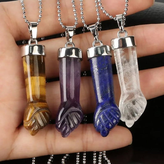 Quatre colliers avec pendentif en forme de poing serré en métal argenté et pierre naturelle - pendentifs et chaines à bille présentés sur une main plate féminine