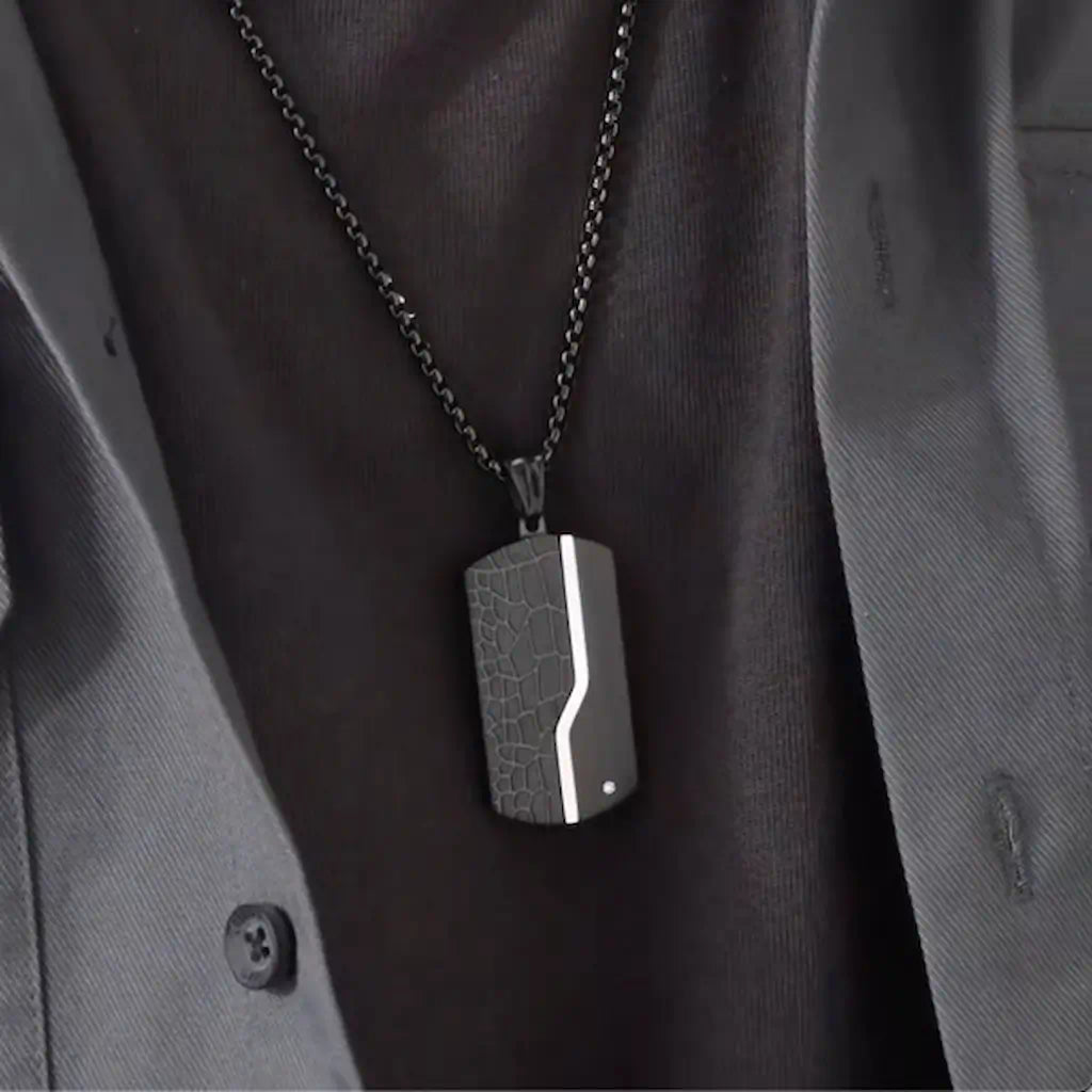 Gros plan du collier Oblong noir porté, avec pendentif moderne en acier porté par un homme vêtu de noir. Présence d'un zircone sur le côté gauche inférieur - coloris acier noir.