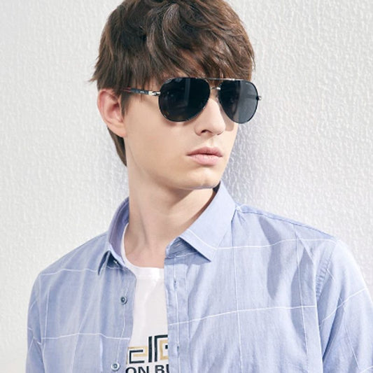 Lunettes de soleil pilote Ari avec verres polarisés et cadre en aluminium sur le nez d'un jeune homme adossé à un mur blanc en crépi - optiques photochromiques, monture or et branche rouge et noir