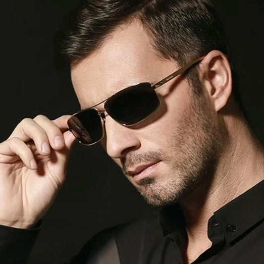 Lunettes de soleil de forme rectangulaire à verres polarisées sur le nez d'un bel homme tout vêtu de noir - cadre en aluminium de magnésium doré- coloris verres gris