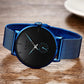Photo d'une montre Top Casual minimaliste reposant sur une table en bois, son cadran, sous-cadran et ses index sont noir - les aiguilles fines et le bracelet en maille milanaise sont de couleur bleu roi