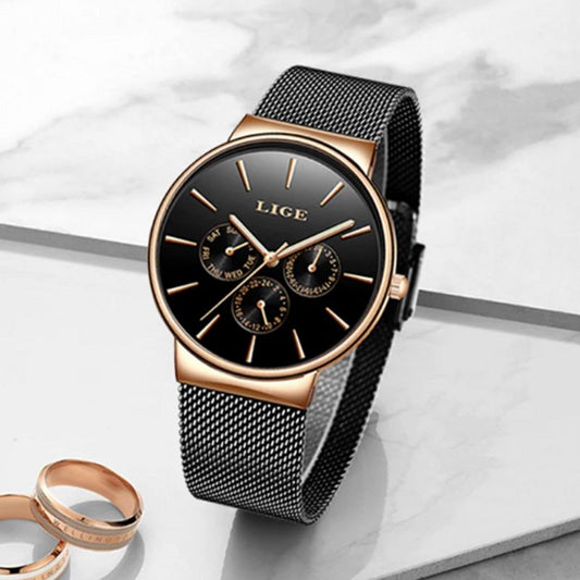 Montre top classe au trois sous-cadrans, date, jour et heure - bracelet maille milanaise de couleur noir, présenté droite sur un plan en vitre opaque au côté de deux alliance en or rose - coloris cadran noir et boitier or rose