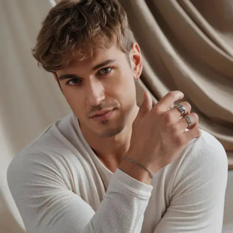 Portrait d'un homme châtain en t-shirt blanc cassé portant des bagues Akrochic en acier inoxydable sur un fond crème raffiné.