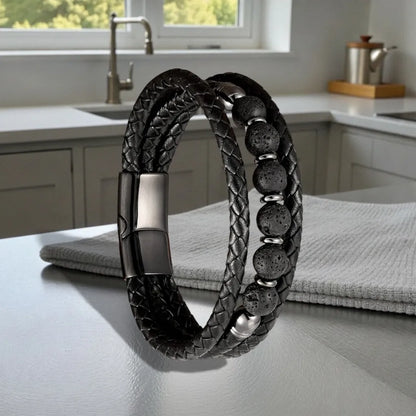 Perspective inclinée du bracelet Vulcan dressé sur une surface satinée, illustrant la souplesse des lanières de cuir texturé et l'alignement géométrique des perles de basalte.