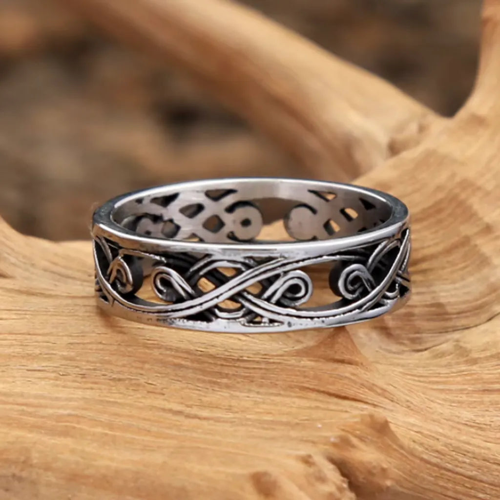 Bague viking en acier inoxydable avec motif celte, posée sur du bois flotté. Anneau argenté avec nœuds entrelacés, style celtique et robuste.