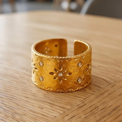 Plan large de face pour la bague Aura en acier inoxydable fusion or. L'anneau ouvert révèle ses motifs floraux et ses éclats de cristal lumineux.