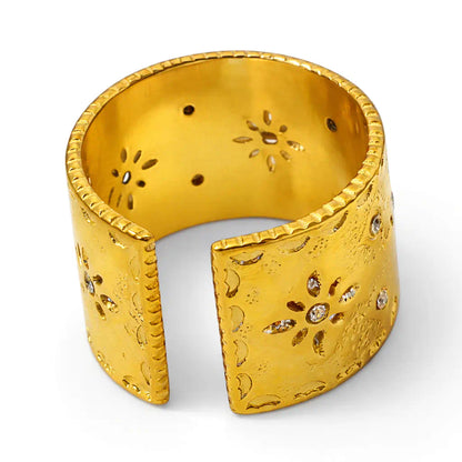 Version à plat de la bague Aura en acier inoxydable fusion or. Ce design boho présente une bande large ajustable ciselée de fleurs et de cristal. Zoom studio fond blanc.