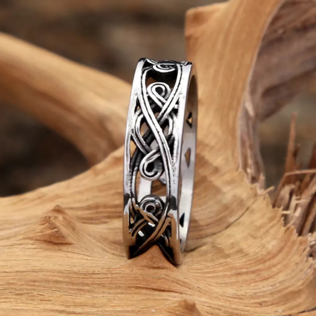 Bague homme argentée avec nœuds celtiques calée et dressée sur du bois flotté, design viking ajouré et robuste, mettant en avant la largeur de l'anneau.