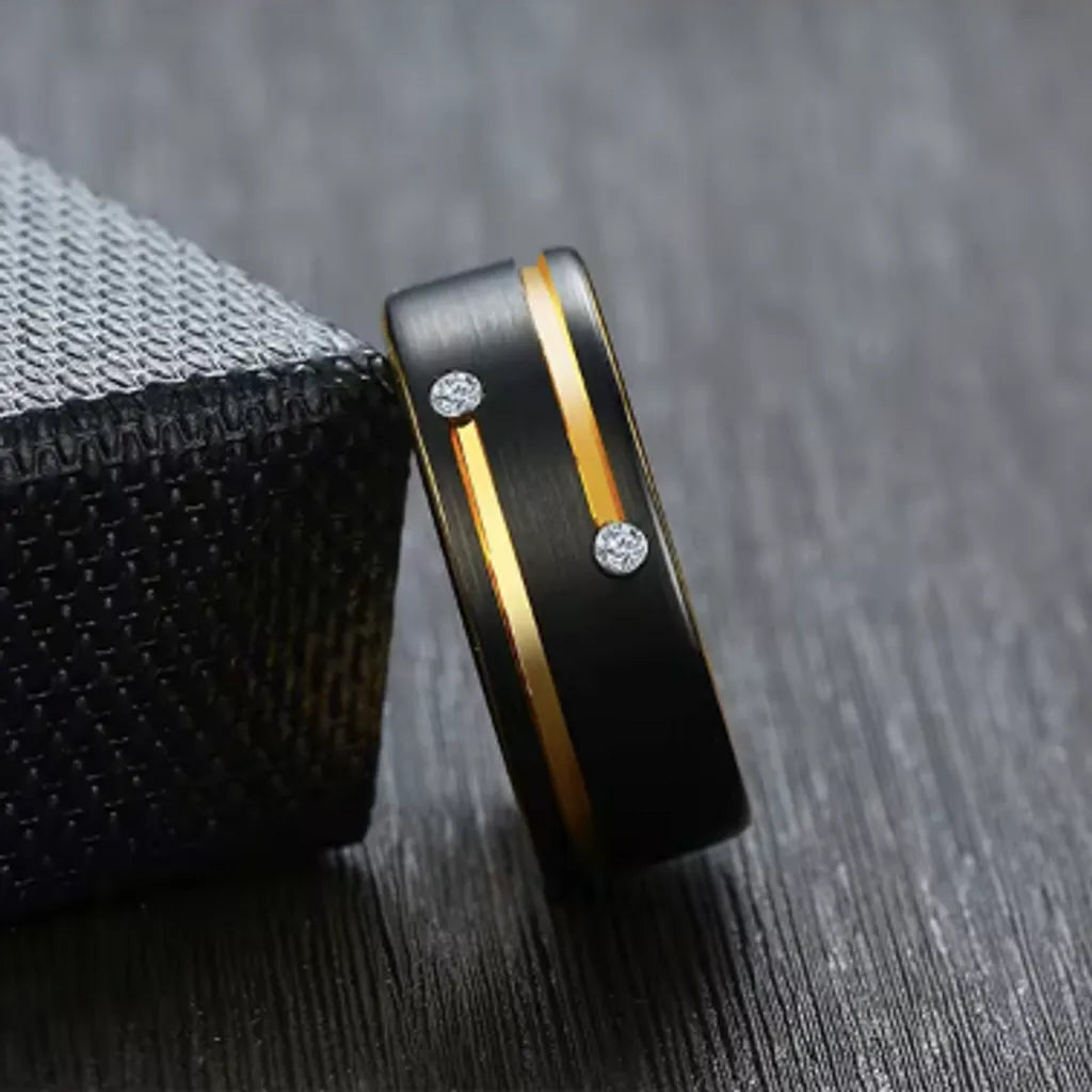 Bague Stella pour homme en tungstène inclinée et posée sur un angle de boite en cuir noir– coloris doré et noir.