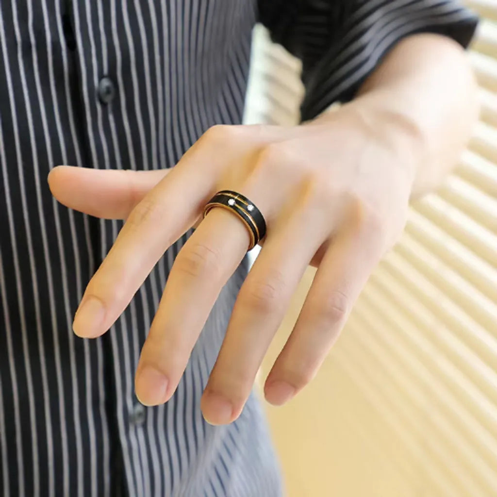 Bague étoile filante - élégance céleste avec star en zircone cubique et rainures dorées sur un anneau en acier inoxydable. Le tout est présenté autour du doigt majeur d'une main gauche d'un homme à la chemise rayée noire et blanche – coloris de la bague noir et or. 