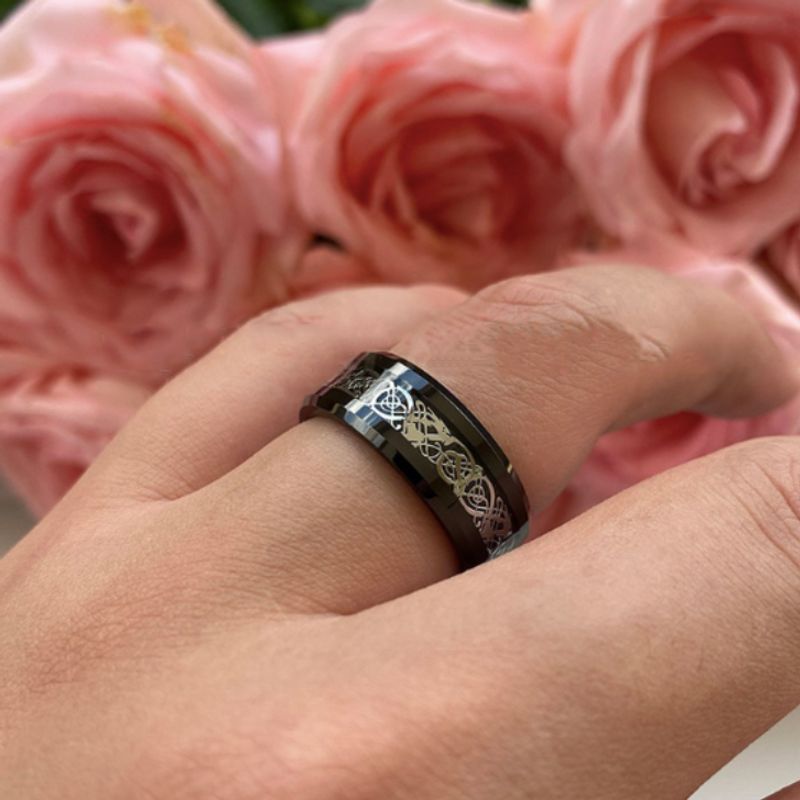 Bague dragon celte pour homme en acier inoxydable, anneau présenté, sur l'annulaire d'une main droite. Fond de l'écran, un bouquet de rose de couleur rose – coloris de l'anneau argent et noir.