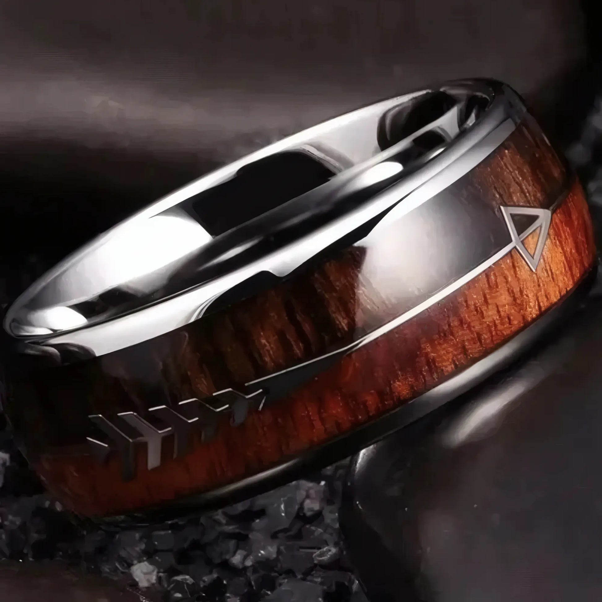 Gros zoom sur la bague Rollo finition acier poli argenté avec flèche incrustée, posée sur galets noirs, contrastes naturels et élégance brute.