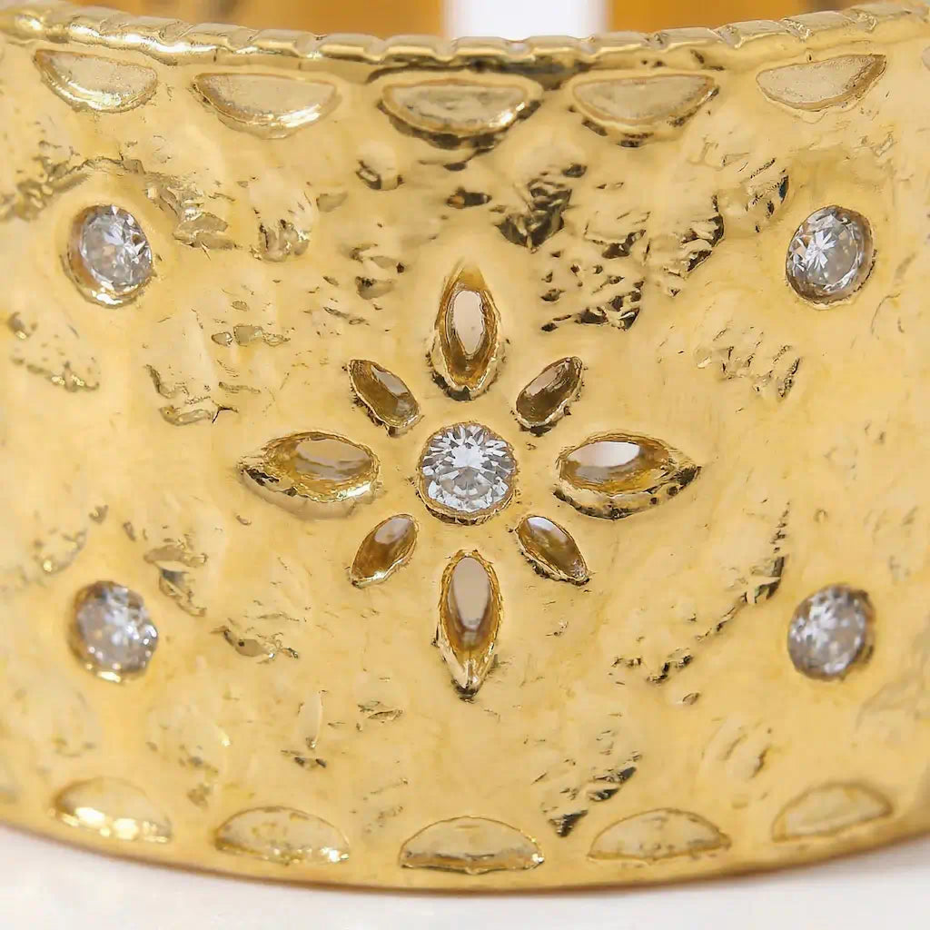 Zoom detail de la bague Lyna ajustable en acier inoxydable fusion or montrant le motif floral central avec petales ajourees et pierre brillante au centre sur texture martellee.