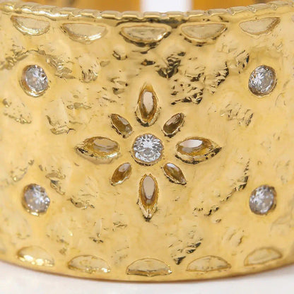 Zoom detail de la bague Lyna ajustable en acier inoxydable fusion or montrant le motif floral central avec petales ajourees et pierre brillante au centre sur texture martellee.