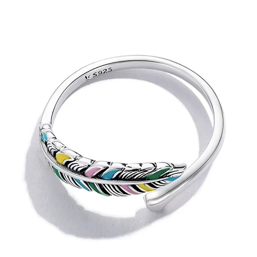 Bague plume colorée en argent 925 et émail multicolore, vue à plat de haut sur fond blanc avec ombre subtile, révélant les détails précis des couleurs émaillées et le design délicat en forme de plume.