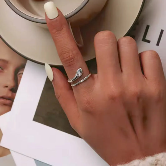 Main féminine délicatement posée sur une tasse de café, ornée d’une bague serpent couleuvre en argent 925. Une touche tendance chic pour sublimer un moment de détente élégant.