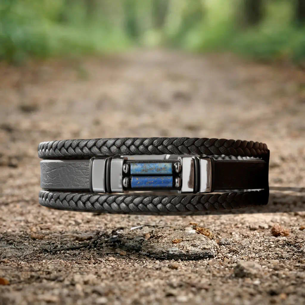 Présentation à plat du modèle Azimut sur la terre brute d'un chemin boisé, où les cylindres de Lapis-lazuli rayonnent au cœur d'une composition organique de cuir souple et de racines.