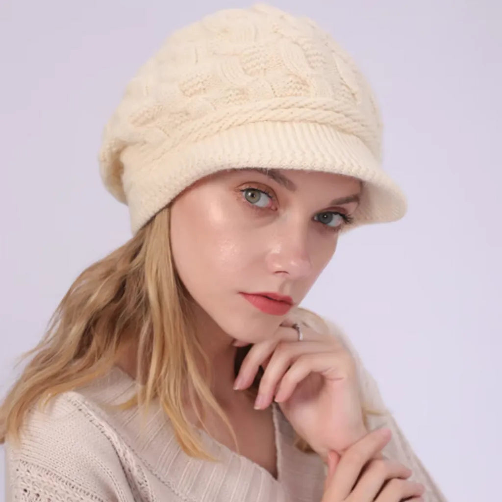 Bonnet pour femme avec visière en laine mélangée, modèle Ashley, porté par un mannequin aux cheveux blonds. Coloris beige Timone avec motif torsadé, offrant un style sobre et raffiné.