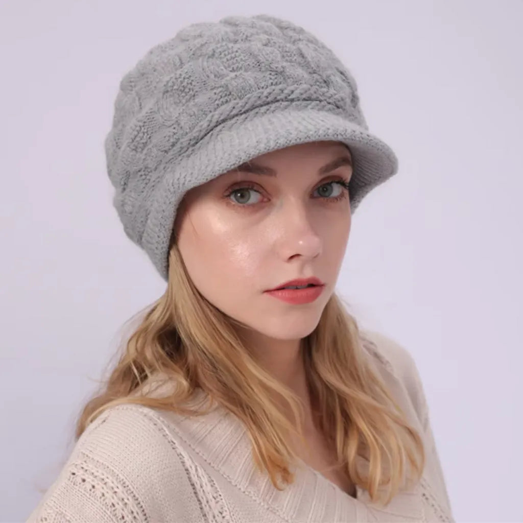 Bonnet pour femme avec visière en laine mélangée, modèle Ashley, porté par un mannequin aux cheveux blonds. Coloris gris avec motif torsadé, pour un look chic et moderne.