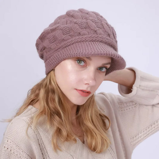 Bonnet pour femme avec visière en laine mélangée, modèle Ashley, porté par un mannequin aux cheveux blonds. Coloris pourpre avec motif torsadé, style élégant et confortable.