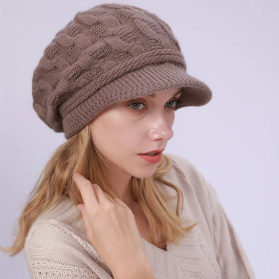 Bonnet pour femme avec visière en laine mélangée, modèle Ashley, porté par un mannequin aux cheveux blonds. Coloris marron avec motifs torsadés, offrant un style chic et décontracté.