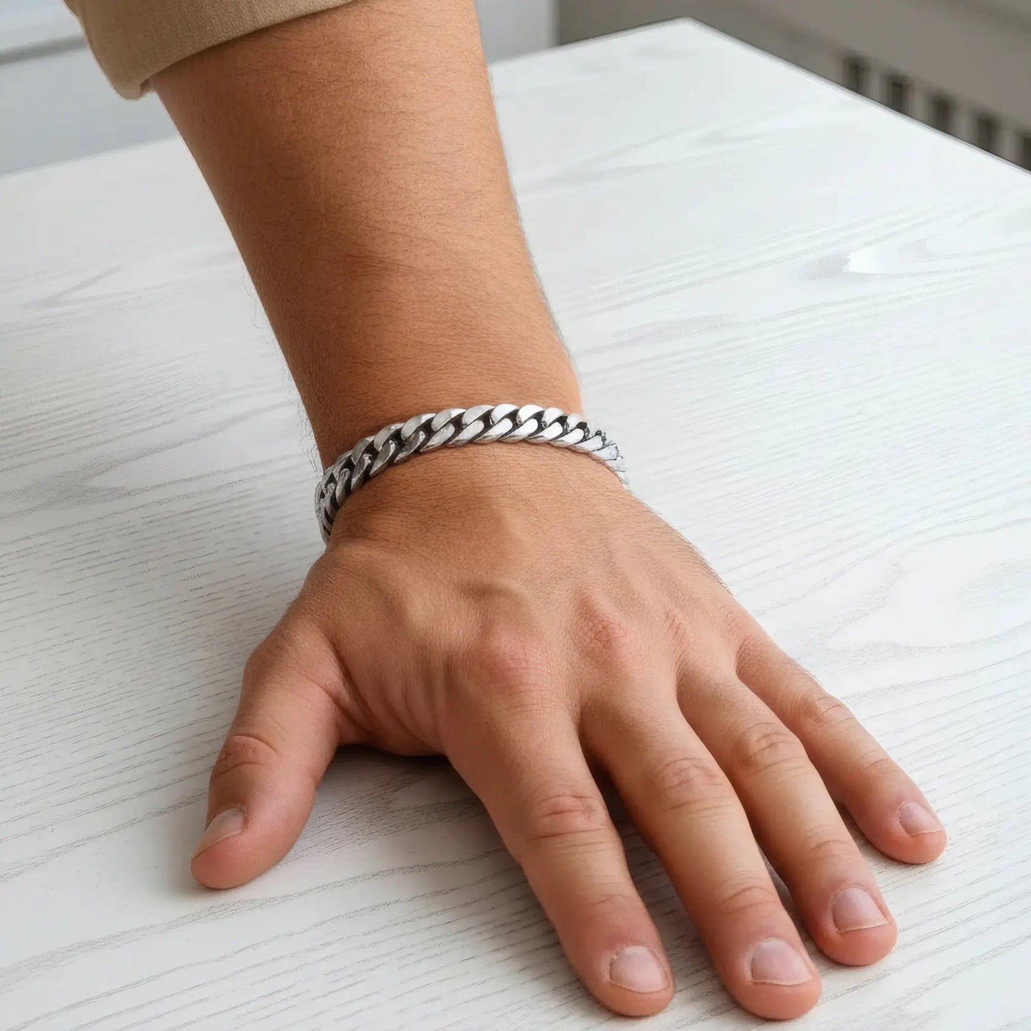 Bracelet maille cubaine acier argenté porté au poignet sur une table en bois clair