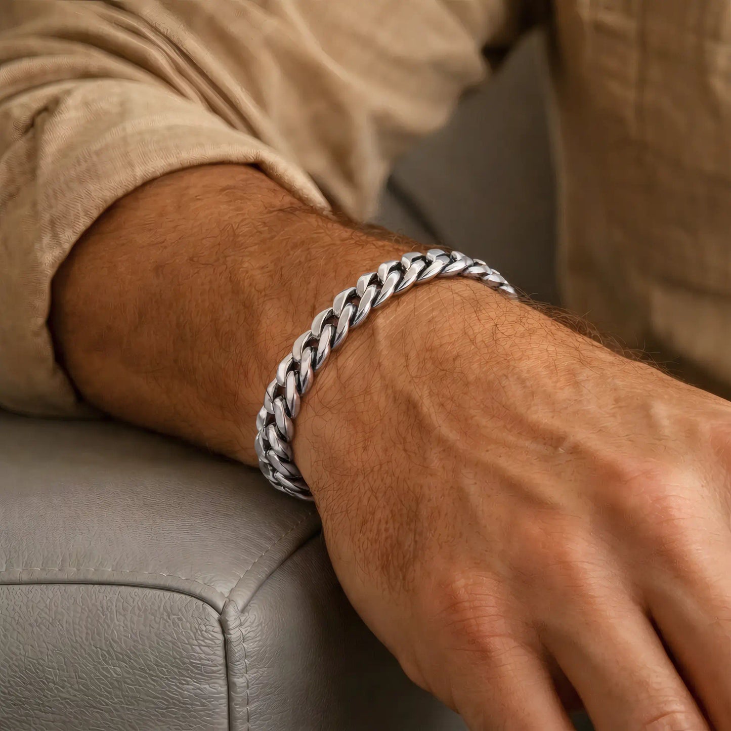Poignet masculin avec bracelet acier mailles cubaines larges posé sur un accoudoir en cuir